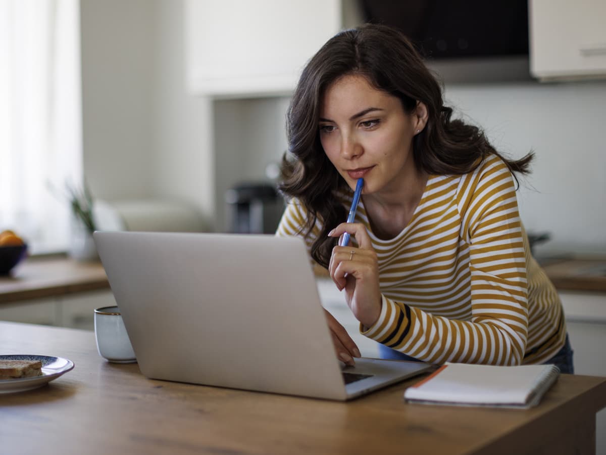 A woman seated at a table, focused on her laptop, with a calm expression in a well-lit room