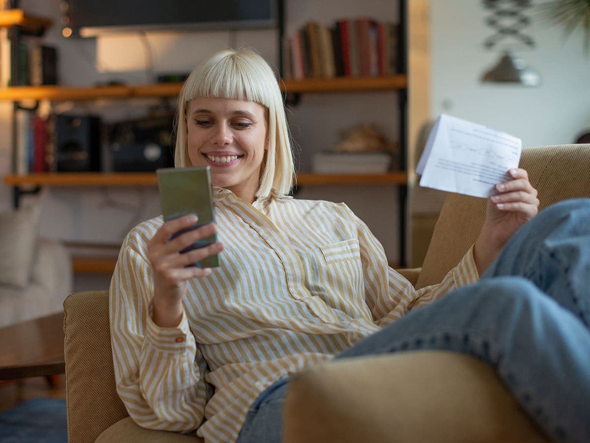 A woman sitting on a couch, focused on writing in her checkbook