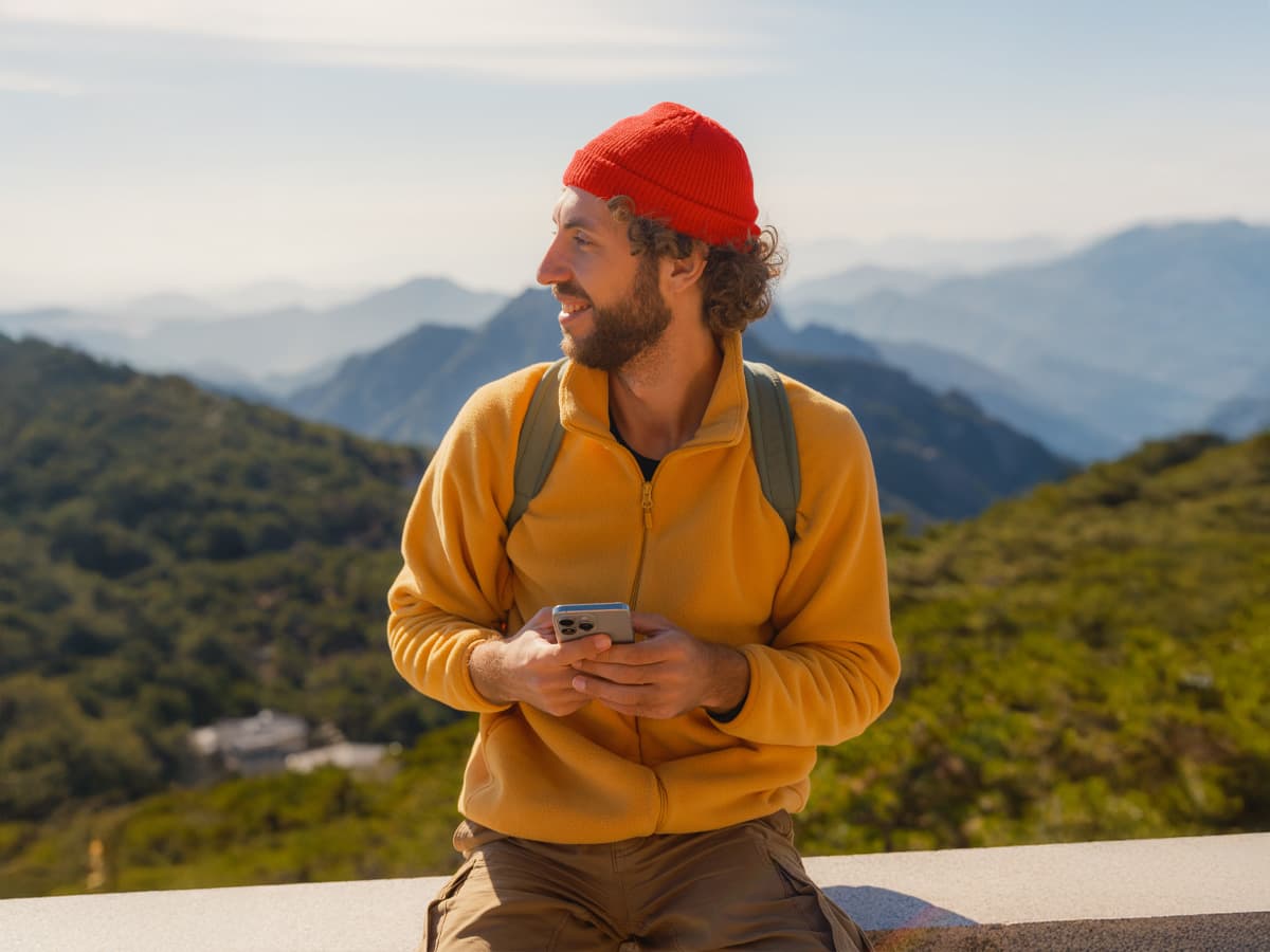 A man casually sitting on a stone wall, looking relaxed in a sunny outdoor setting